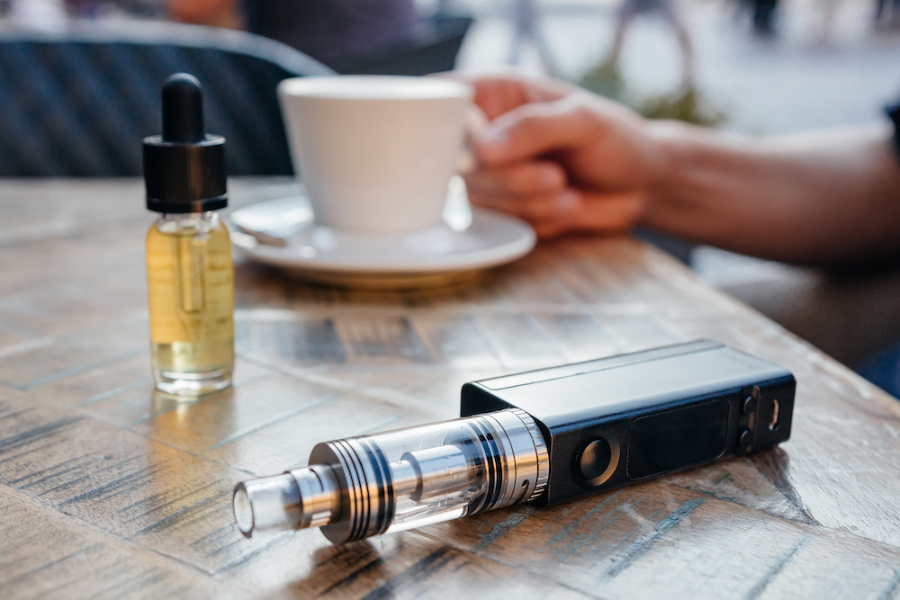 man using vaporizer or electronic cigarette and drinking coffee